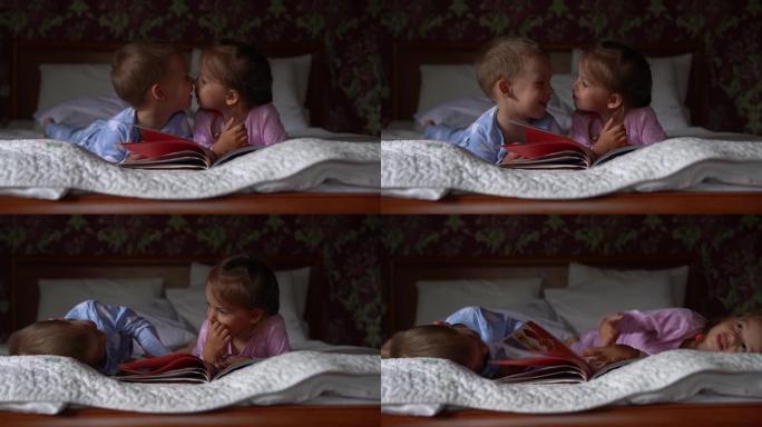 两个可爱的微笑的preshool，穿着睡衣的蹒跚学步的孩子在床上读童话书。兄弟姐妹小双胞胎读者玩得开