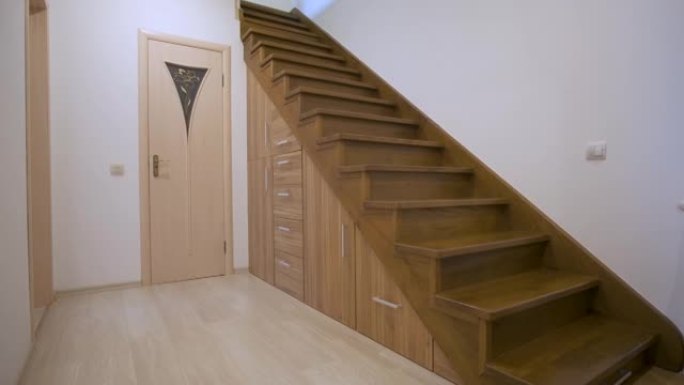 现代建筑内部，豪华走廊，多层住宅中有光滑的木制楼梯。定制的拉出式橱柜在楼梯下的插槽中滑行。使用空间进