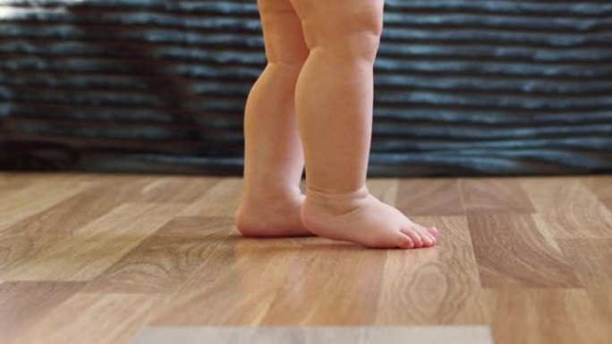 婴儿的小腿在地板上迈出第一步，特写腿，侧视图。婴儿在镶木地板上迈出了一步。家庭概念