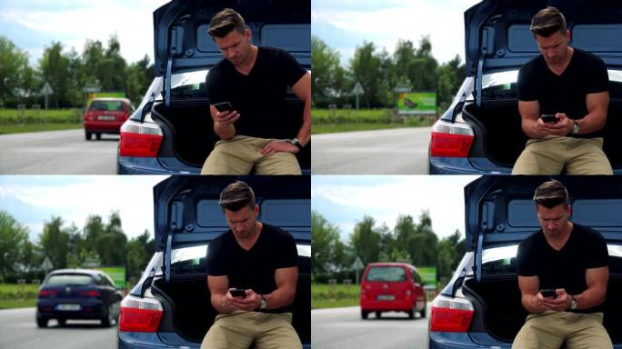年轻英俊的男人坐在汽车后备箱里，在智能手机道路上工作 (打字)，背景是过往的汽车