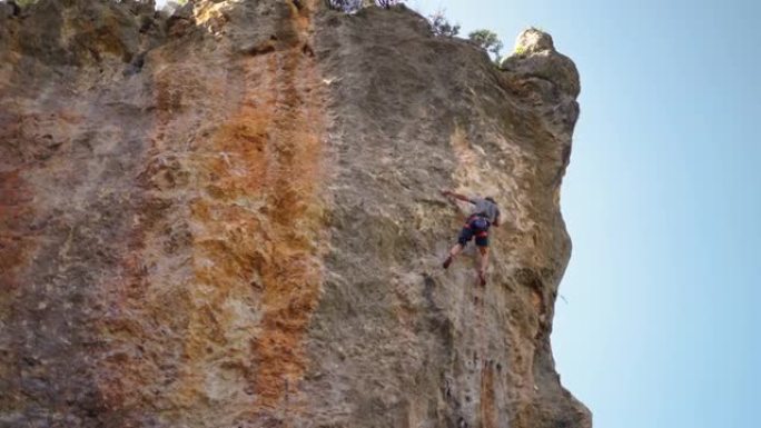 强壮而熟练的男子登山者通过具有挑战性的路线在垂直的石灰墙岩壁上攀登，做出了几次艰苦的自信努力，失败和