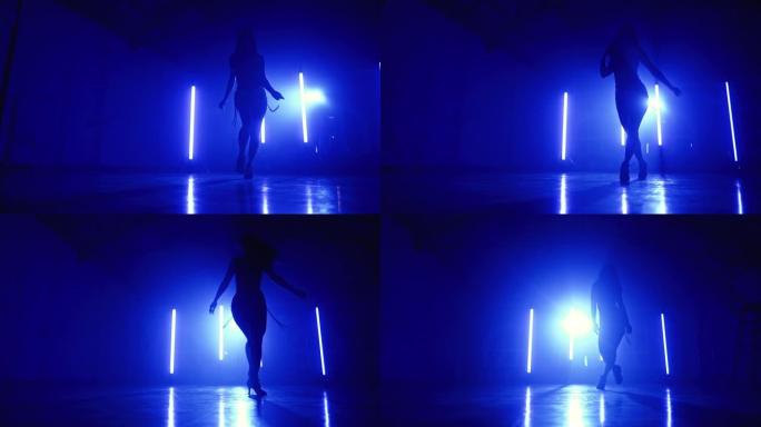 穿着性感服装的年轻女子在带长灯的蓝色工作室里，可塑性地欣赏音乐。女士独自表演。性舞蹈、艺术的概念