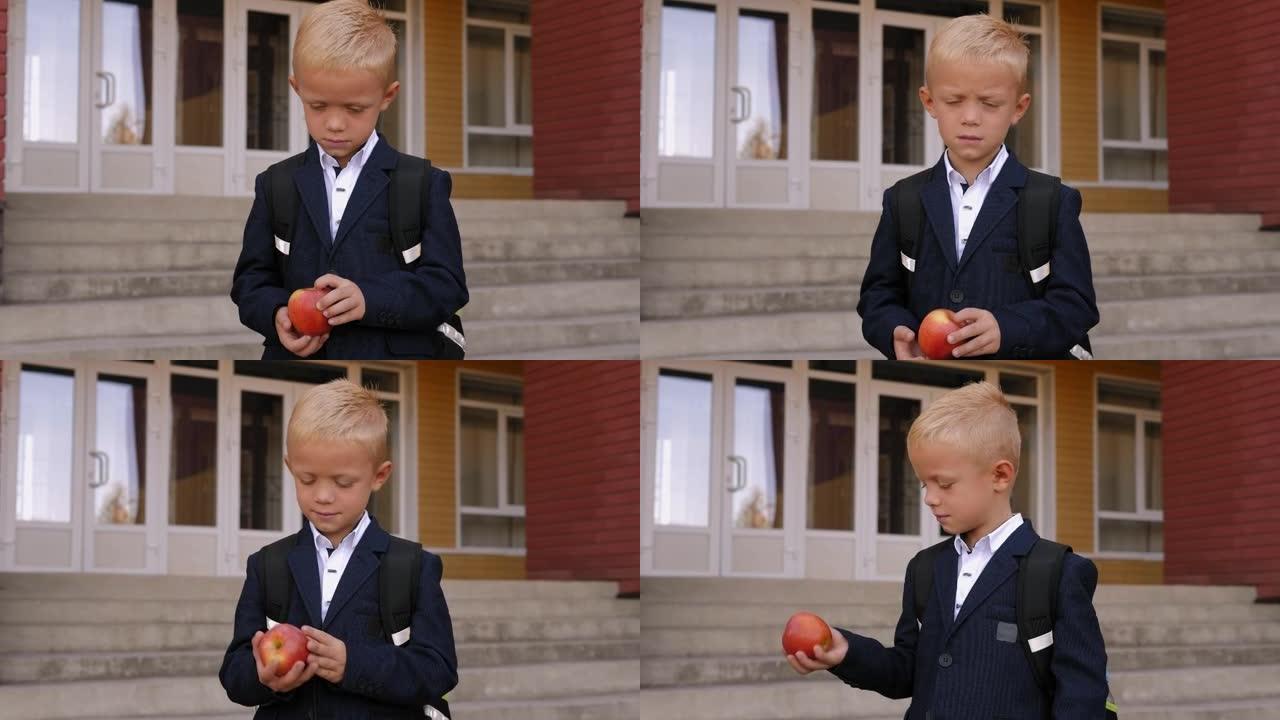在学校附近，一个男孩背着背包，手里拿着一个红苹果的特写镜头
