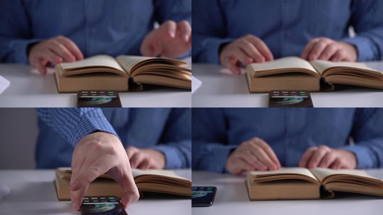 一个男人的手拿着一本书，拿着智能手机放在白色的桌子上特写。