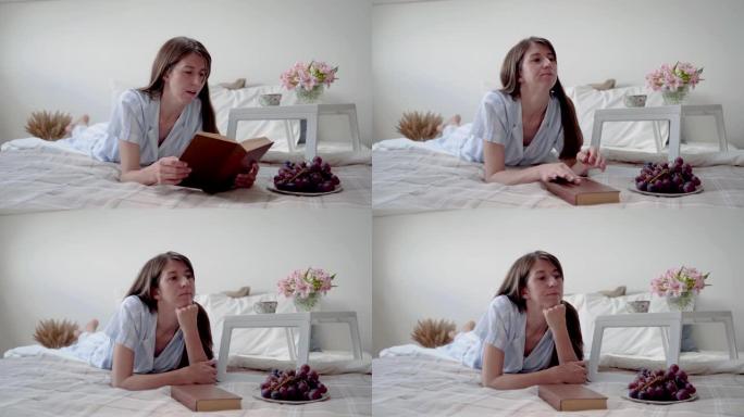 一个女人躺在床上看书。女人做梦。床头柜上摆着鲜花和一杯咖啡。在家休息。反思。女人穿着漂亮的睡衣。床上