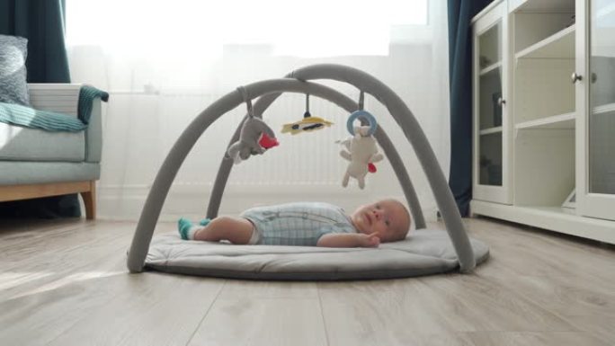 婴儿躺在带悬挂玩具的软游戏垫上，可爱的男婴在活动健身房玩伴上玩有趣的动物，客厅地板上2个月大的新生婴