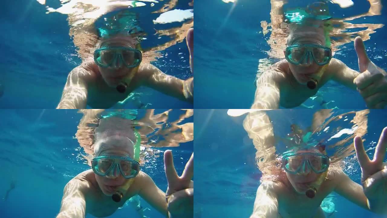一个戴着面具和通气管的男人在海水下挥舞着手，向Victoria GoPro展示手指