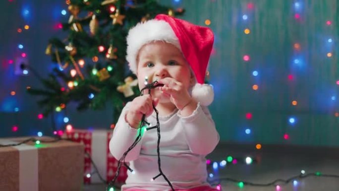 平安夜。戴着圣诞帽的可爱的小孩的肖像，咀嚼着节日的灯光。慢动作。新年假期的概念