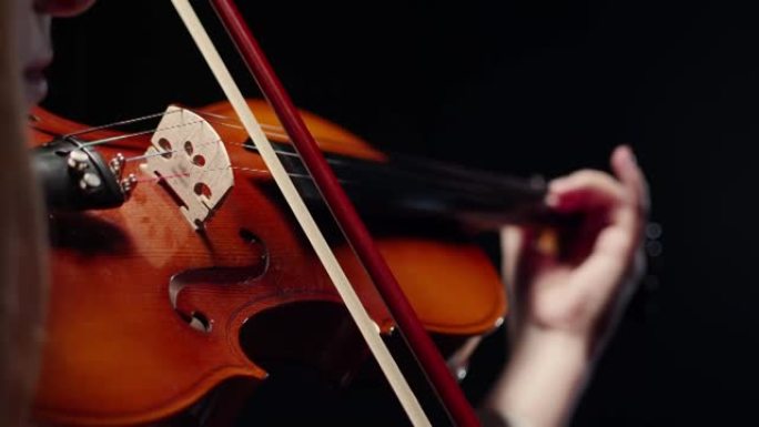 女小提琴手在小提琴的琴弦上握着弓，在黑暗的工作室里演奏古典音乐，特写镜头。交响音乐的概念和表演