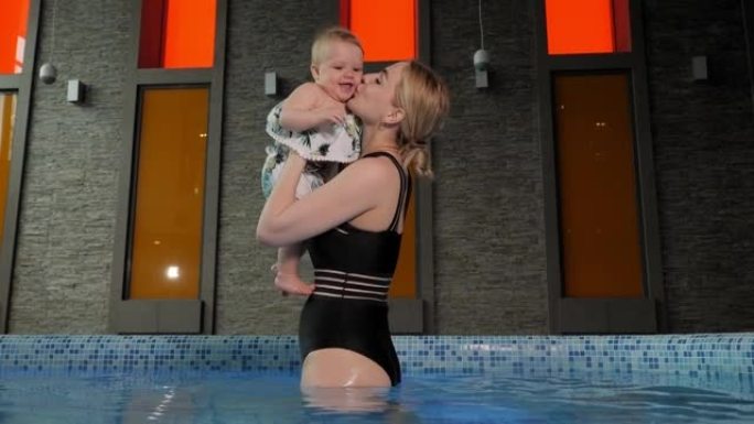 一位年轻的有爱心的母亲在游泳池里亲吻她的小女儿。