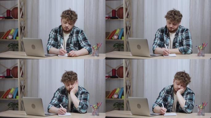 穿着方格衬衫的年轻人看着笔记本电脑屏幕无聊，在笔记本电脑上做笔记。留着胡子的红发男性坐在家庭办公室的