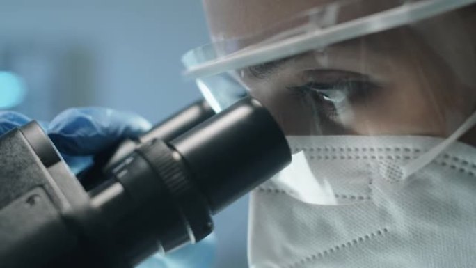 穿着防护服的女实验室科学家通过显微镜观察