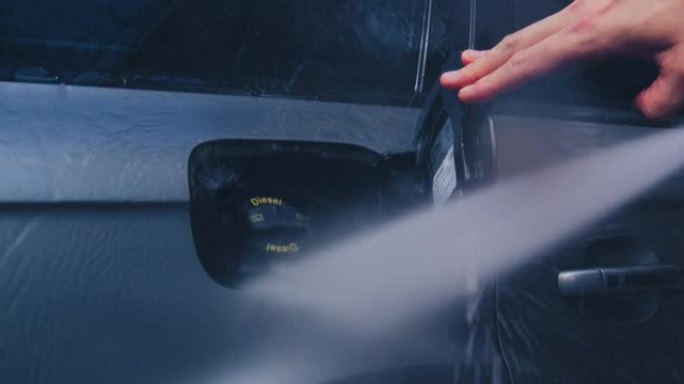 外部汽车细节。洗车工人使用高压清洗机在汽车上喷水，清洗油箱以获得光泽