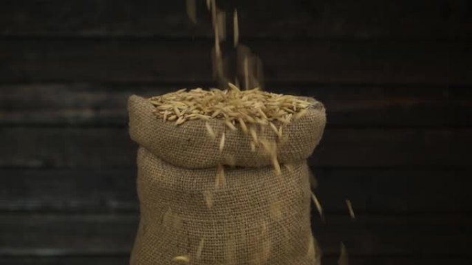 慢动作。在木墙的背景下，将燕麦颗粒倒入满袋中。