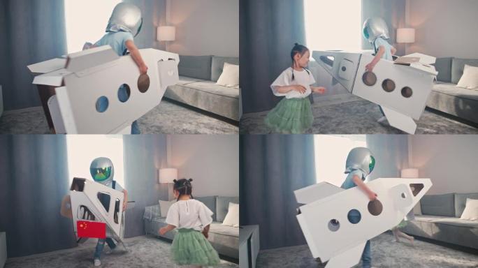 中国孩子在房子的客厅里玩耍，一个穿着宇航员服装的男孩在玩纸板航天飞机，一个可爱的女孩姐姐在房间里追赶