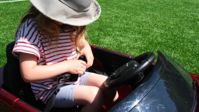年轻女孩解开坐在小玩具车里的安全带