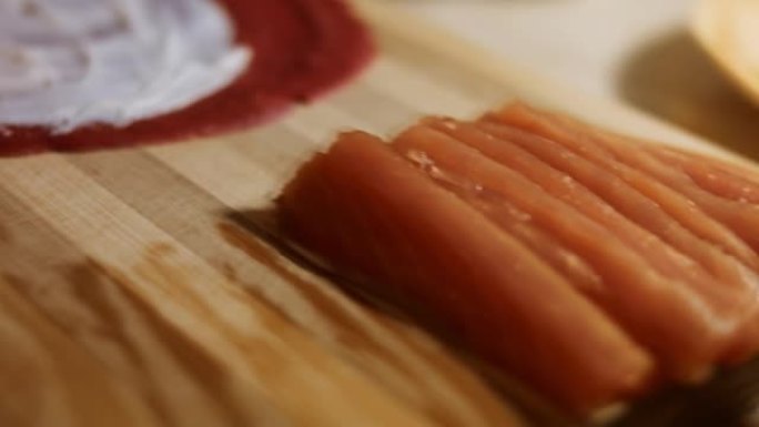 薄薄的美味彩色煎饼。女人的手的特写镜头，将鲑鱼片放在木板上涂上奶油奶酪的红色煎饼上。滚动煎饼。慢动作