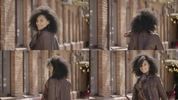 年轻的非洲裔美国妇女走在街上，转身微笑。穿着棕色皮夹克的黑发女人在模糊的砖砌建筑中摆姿势。特写。慢动