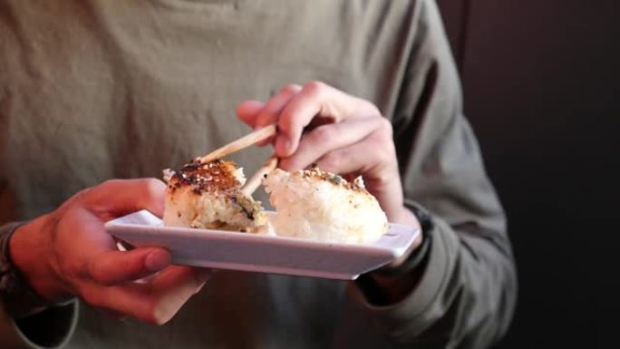 特写镜头，男子用筷子吃烤饭团的手持镜头