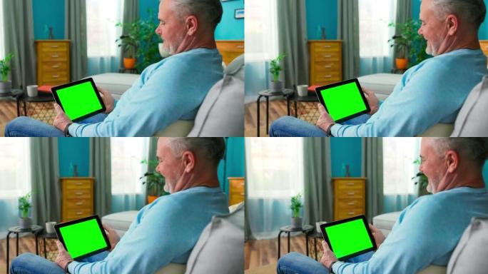 老人从平板电脑在线流媒体服务中选择电影。观看系列与点播视频网站概念。带有空白绿色模拟屏幕显示的数字平