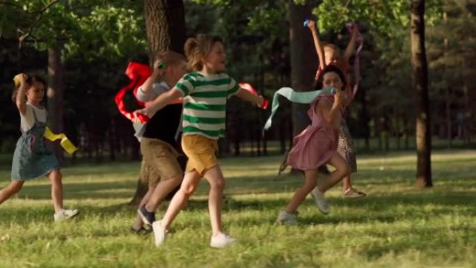 五名兴奋的孩子手拿彩虹彩带，在公园草地上奔跑，快乐地尖叫。儿童庆祝自由和平等的慢镜头