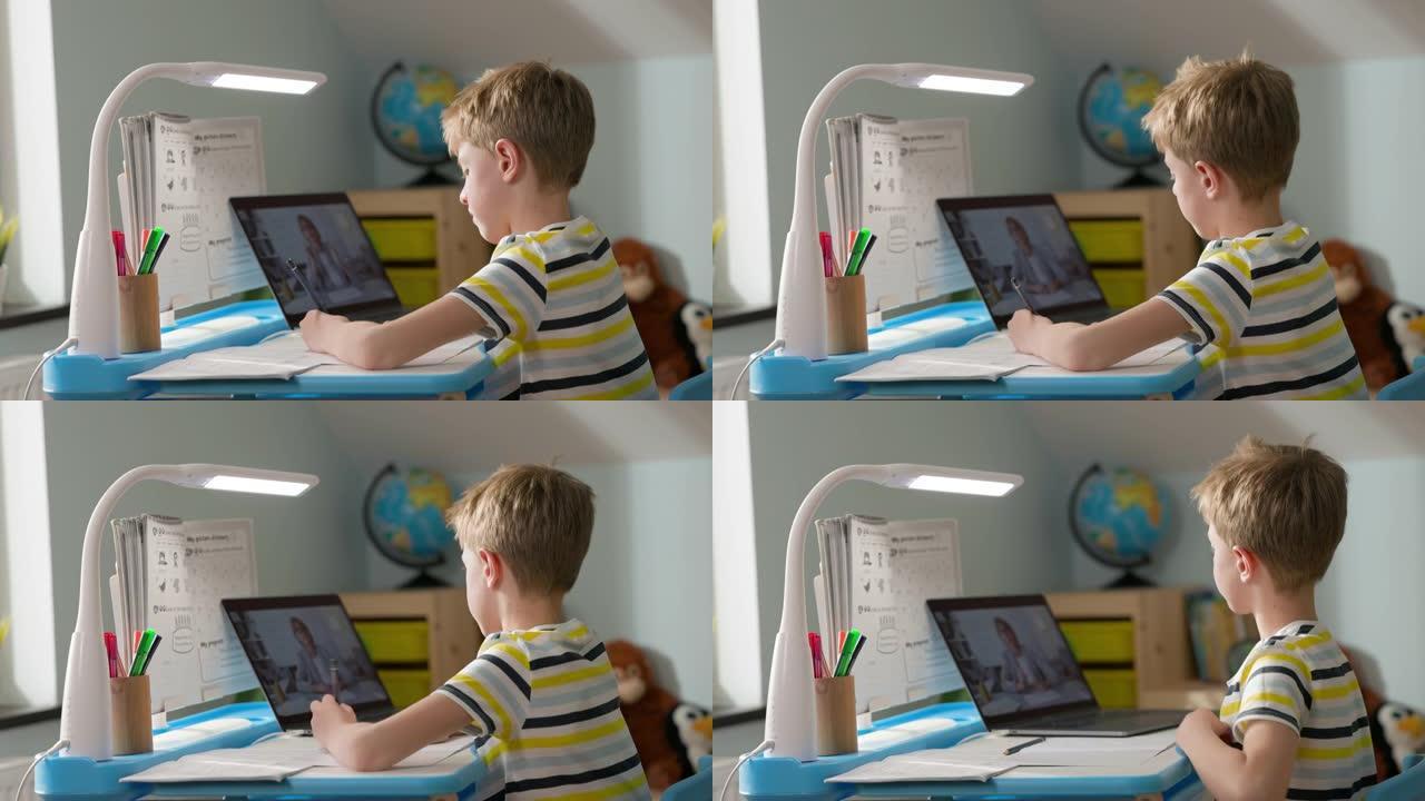 男孩坐在家里的笔记本电脑上。在线课程。孩子一边看笔记本电脑屏幕，一边写笔记本电脑。