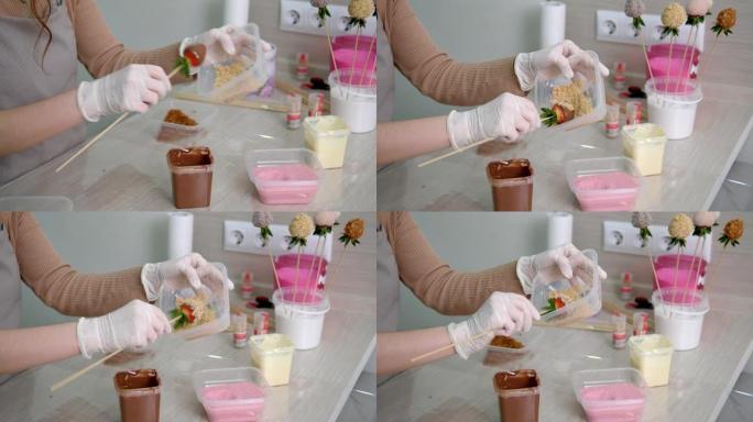 一个戴着白手套的女孩在牛奶巧克力和磨碎的核桃中准备草莓