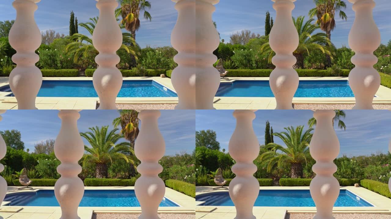 摄像机从左到右，向侧面移动，露台的石柱，别墅的阳台，俯瞰美丽的游泳池。供游客参观的有棕榈树的花园。