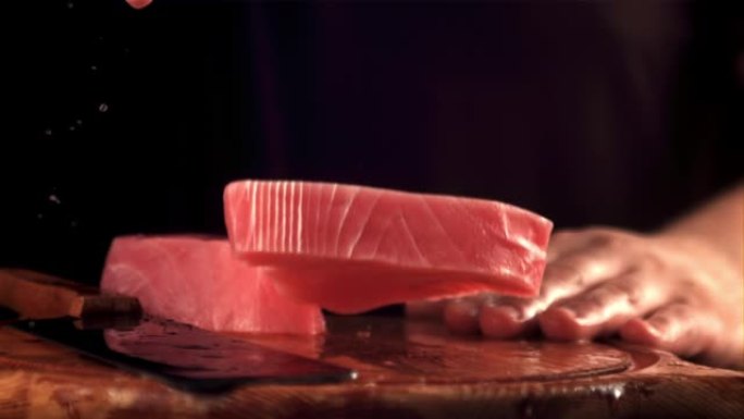 该男子的超慢动作手将生金枪鱼牛排扔在切菜板上。以1000 fps的速度在高速摄像机上拍摄。