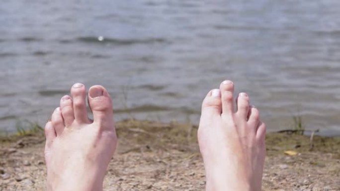 女人脚日光浴在沙滩上的河流，靠近水