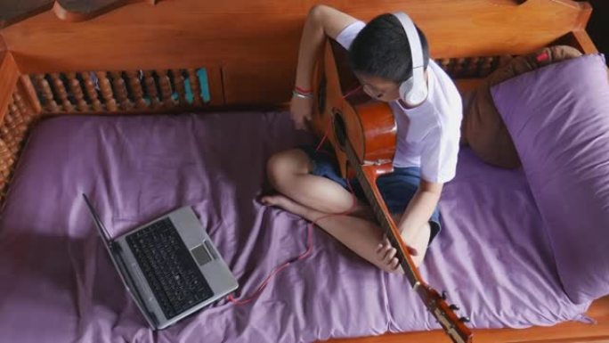 男生在家在线学习吉他练习。