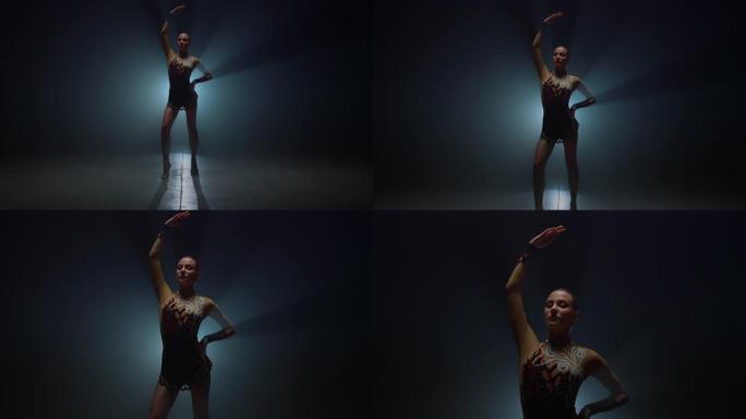 体操女孩举起手站在黑暗的空间。女运动员在室内摆姿势。