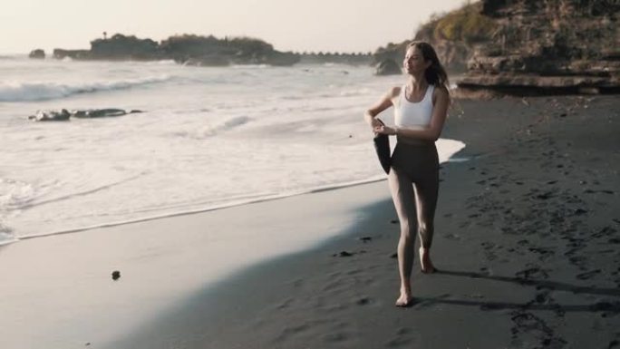 穿着运动服的快乐女人沿着黑沙滩散步，微笑着转身