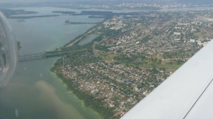 一架小型客机舷窗靠着白色机翼的视野。大都市的俯视图是第聂伯河沿岸的一条大绿色河流，其中建造了房屋和桥