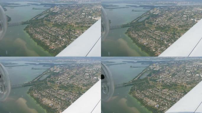 一架小型客机舷窗靠着白色机翼的视野。大都市的俯视图是第聂伯河沿岸的一条大绿色河流，其中建造了房屋和桥