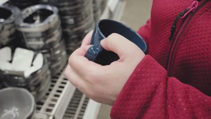 戴着手套对抗病毒的女孩在商店里买了蓝色杯子用来喝热茶和咖啡