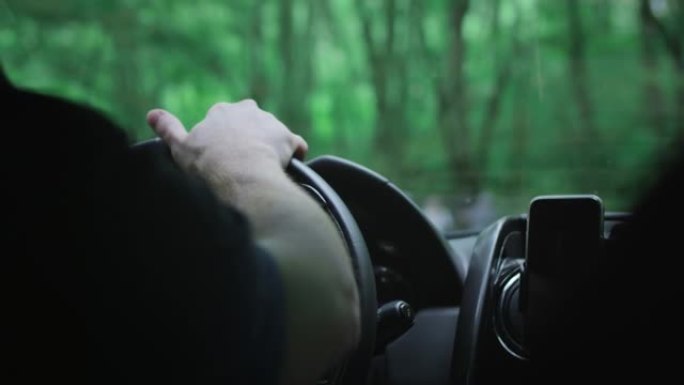 一位老人在绿色的森林里开车。皱巴巴的手中的黑色皮革方向盘的特写镜头。