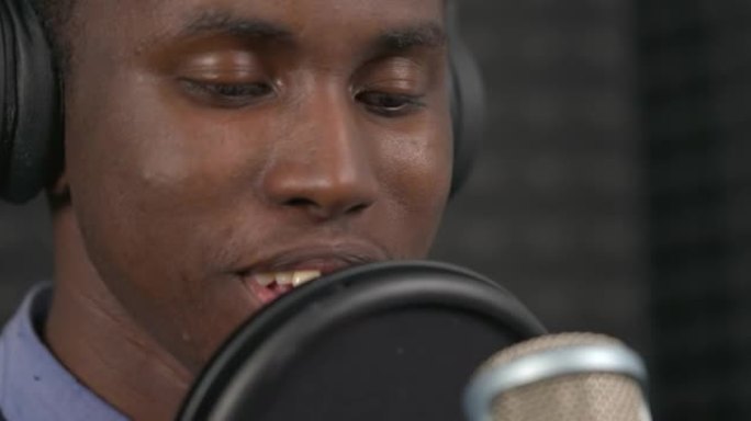 非洲歌手在专业录音机工作室的耳机表演抒情歌的宏观特写镜头。背景模糊