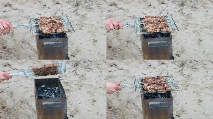 男人的手在沙滩上的烧烤架上煮肉。晴天在便携式烤架上烧烤烧烤