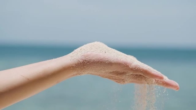 女人从手上吹沙子，沙子从手指里倒出来。沙子从手掌中张开的手的细节