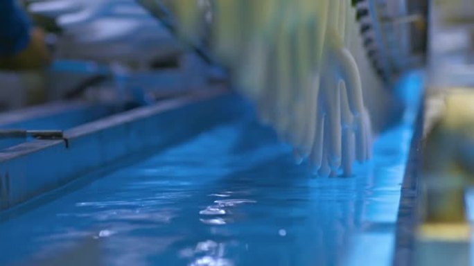 在工厂的传送带，将橡胶医用手套的坯料浸入液体溶液中，冲洗模具。准备制造橡胶手套，现代化设备。4k，普