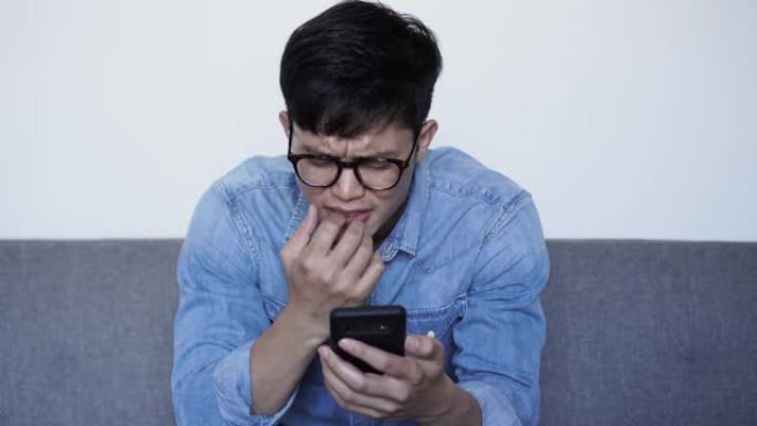 特写场景年轻的亚洲男子在阅读评论或阅读社交媒体或网站上的假新闻或智能手机上的虚假新闻时皱着眉头，对生