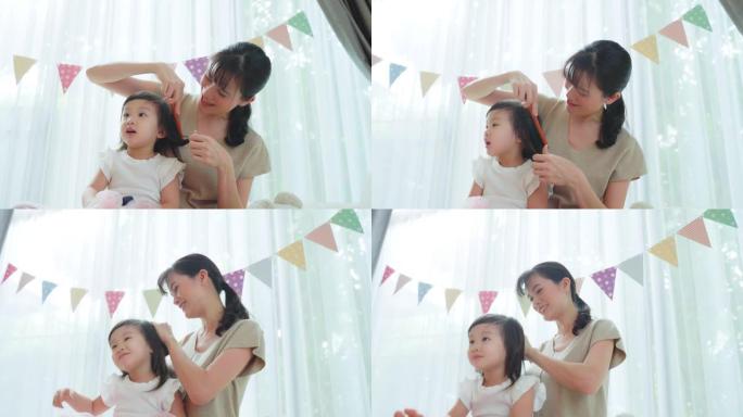 亚洲慈爱的母亲和年轻的小女孩女儿在家里的客厅里度过闲暇时光。有爱心的妈妈用温和的发刷梳理小孩的头发。