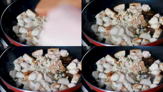 用切碎的大蒜煮熟并用油和香料油炸的鸡肉块的宏观特写镜头，在平底锅中进行鲜肉烹饪过程的特写镜头