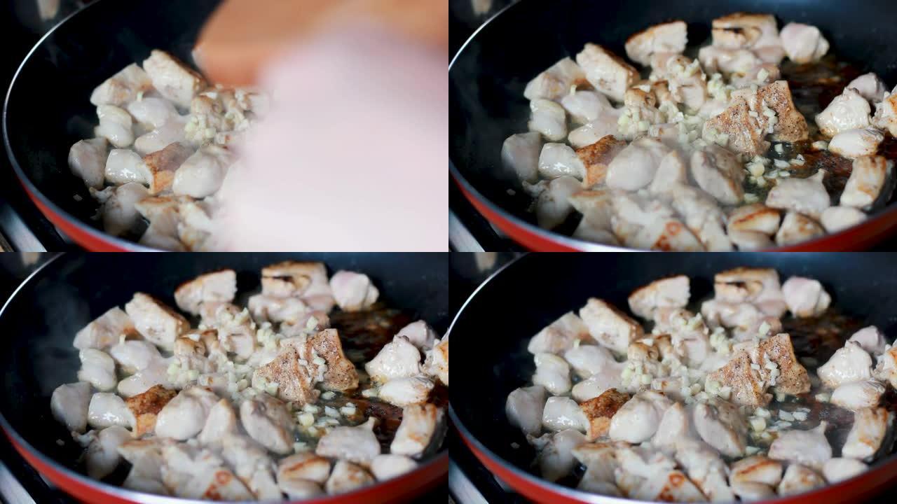 用切碎的大蒜煮熟并用油和香料油炸的鸡肉块的宏观特写镜头，在平底锅中进行鲜肉烹饪过程的特写镜头