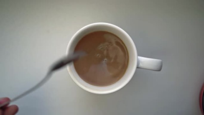 男人的手将咖啡与奶油或牛奶与勺子混合。