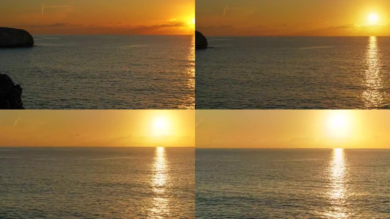 早晨橙色的太阳升起在平静的海面上，左边是多岩石的海岸，延时视频