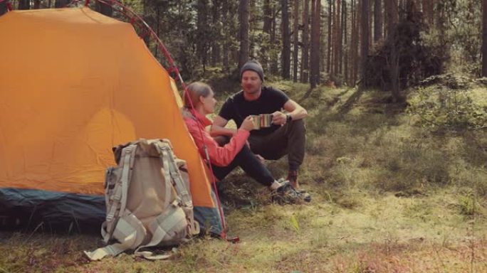 露营之旅-徒步旅行后，年轻夫妇在森林营地的帐篷旁休息。主动旅行