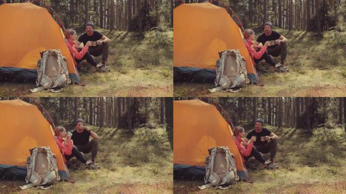 露营之旅-徒步旅行后，年轻夫妇在森林营地的帐篷旁休息。主动旅行