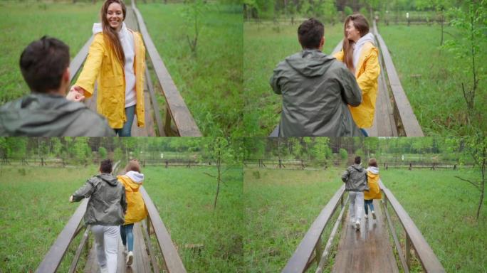 浪漫的年轻夫妇在乡村的木路上慢动作奔跑。快乐的爱心女人牵着男朋友的手，男人在雨中跟着她去森林